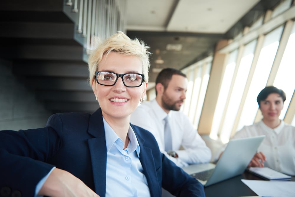 blonde with short hairstyle  and glasses,  business woman on meeting, people group in background at modern bright office indoors blonde with short hairstyle  and glasses,  business woman on meeting, people group in background at modern bright office indoors