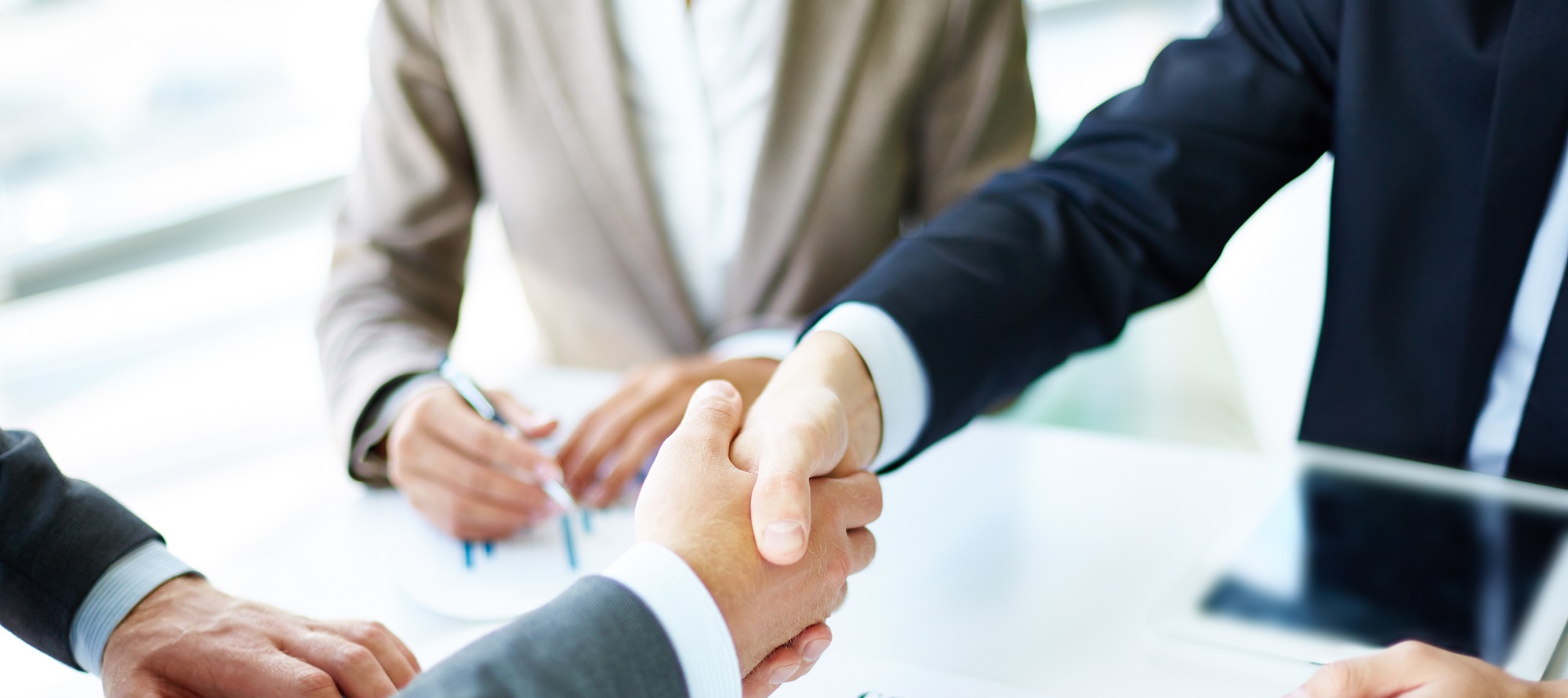 image-of-business-partners-handshaking-over-business-objects-on-workplace-min